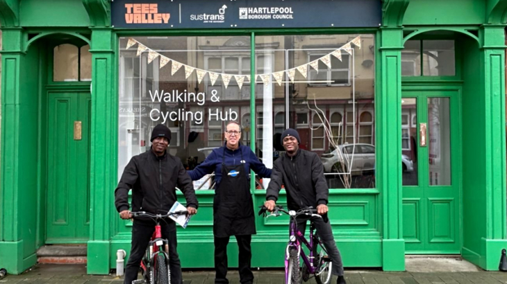 Three men stood smiling outside of one of Walk Wheel Cycle Trust's walking and cycling hubs in Tees Valley two of the men have cycles
