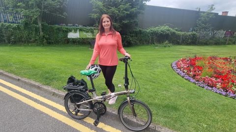 Woman in pink standing with a foldable bike in park