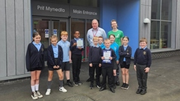 Pupils and staff from Ysgol yr Hafod stand looking at the camera with their Active Travel School Award outside the school entrance.