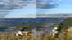 Someone sitting on grassy hillside with bike behind them, looking out on Welsh valley with quarry below