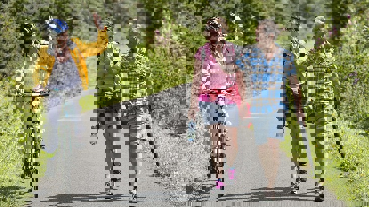 Cyclist passing two walkers on cycle path, both parties waving to each other