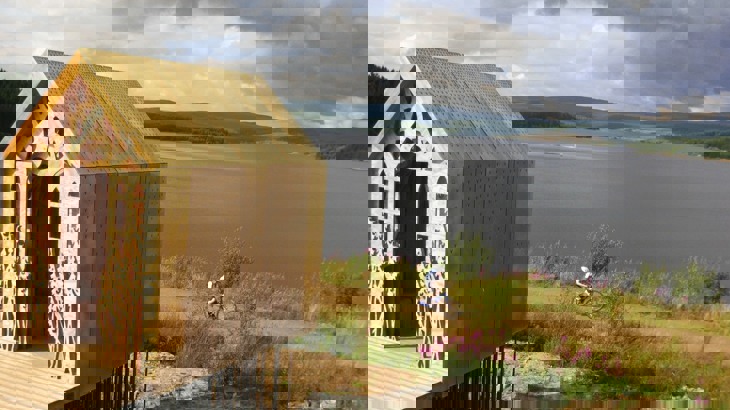 Wooden shed with carvings on the front overlooking cycle path with cyclist on it and lake