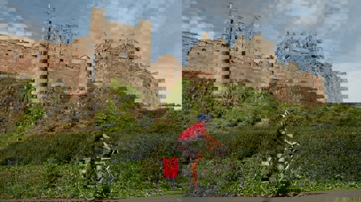 Cyclist with helmet and panniers cycling passing brown brick castle