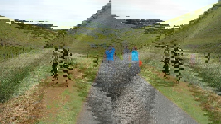 Group of touring cyclists on tarmac path through grassy valley