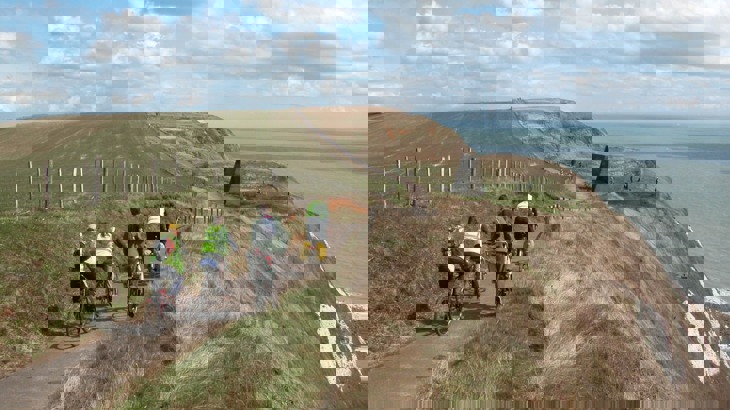 Group of touring cyclists on tarmac path  on cliff with white chalk to the side