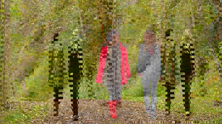 Two women walking on path strewn with fallen leaves through woods