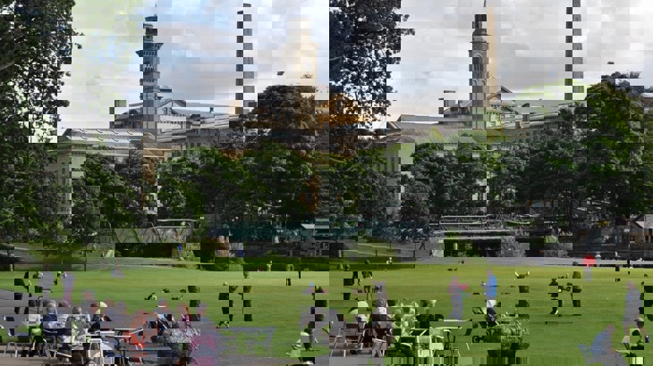 Old industrial building with green, outdoor cafe seating area and metal sculpture of a lama 