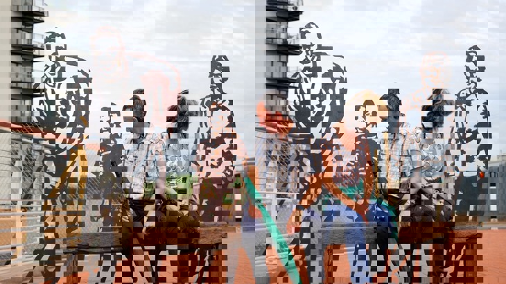 Couple sitting on bench in front of metal artworks shaped like people's silhouettes 