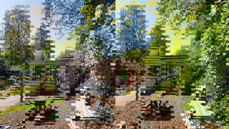 Wooden cafe building with wooden benches out the front and trees to the side