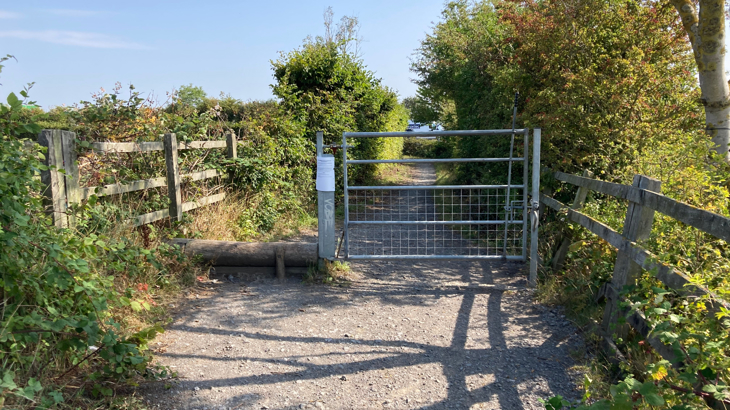 A traffic free National Cycle Network route on a sunny day with shrubbery either side and an access gate in the middle of the path
