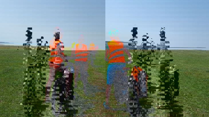 girls on bikes in Walk Wheel Cycle Trust hivis on a grass hill with blue skies