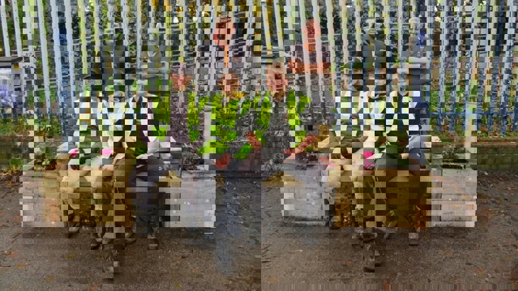 College students and tutor at railway station, sitting on bench planter.