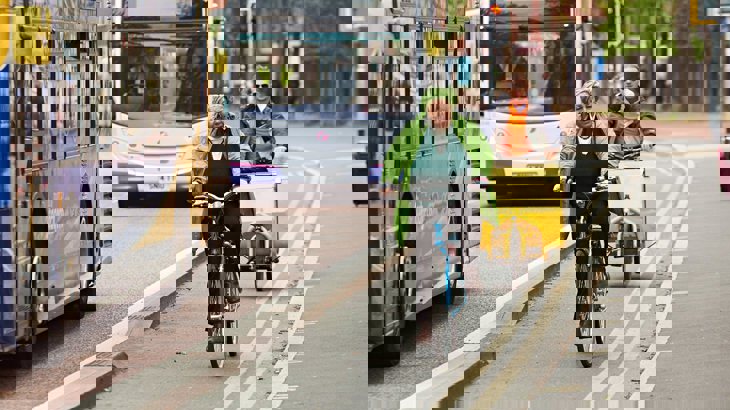 People cycling along a segregated cycling lane next to double-decker buses in a UK city