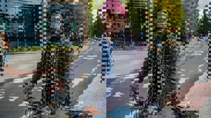 Man wearing a beanie standing with his bicycle smiling at the camera on quiet London street