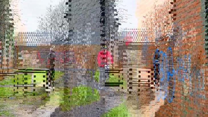 A person cycling past a very small gap next to a barrier on a National Cycle Network route in the rain