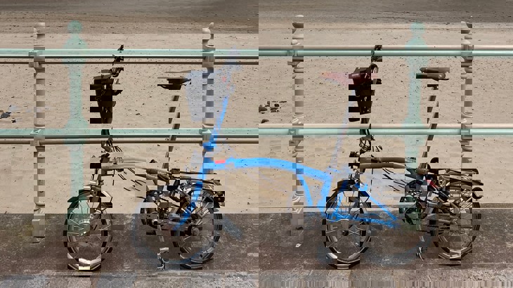 Tierney's blue e-bike propped up against a green railing along the coast with beach in background
