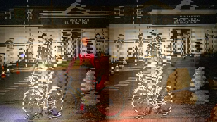 Tom standing with his bike and helmet in front of Lands End at 4am in the morning