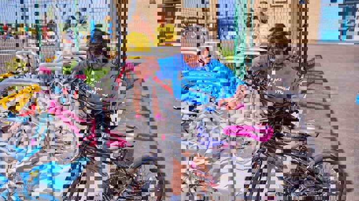 A girl in a blue t-shirt locking her bike to a Sheffield cycle stand in the school playground