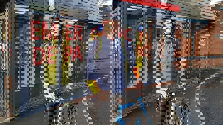 Doctor Matthew Jackson wearing lycra leggings, a waterproof jacket and a helmet, standing with his bike outside his GP surgery
