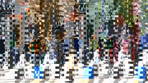 Two women smiling and chatting as they cycle together along a new temporary cycle lane through the high street.