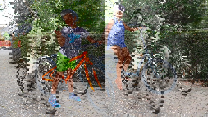 Mum and son smiling and giving a thumbs up as they stand with their bicycles in a park.