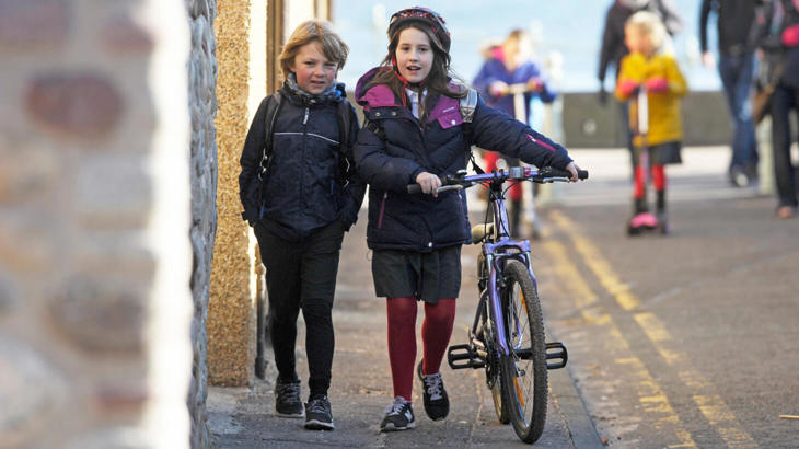 two children walking down road with a bike