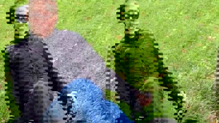 Kelly, wearing a black jacket and blue jeans, sitting on her ICE trike - an adapted bicycle - smiling at the camera.