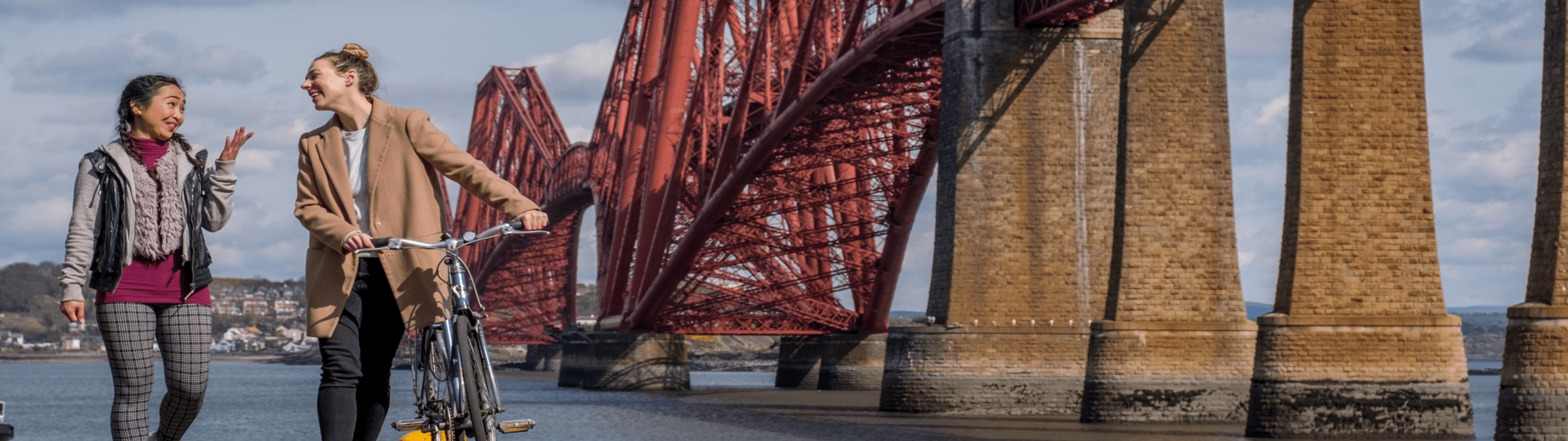 two people walk and cycle past the Forth Road Bridge between Edinburgh and Fife