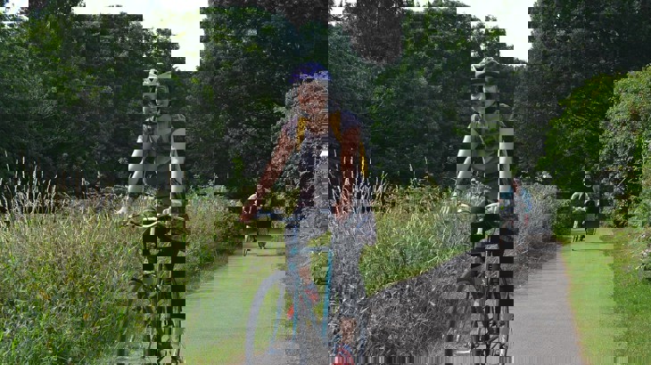 Our West Midlands partnerships manager, Ridhi Kalaria cycling along a traffic-free path in England, wearing her helmet and smiling.