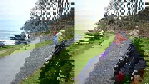 A cyclist on the North Down Coastal Path watched by two people sitting on a bench 
