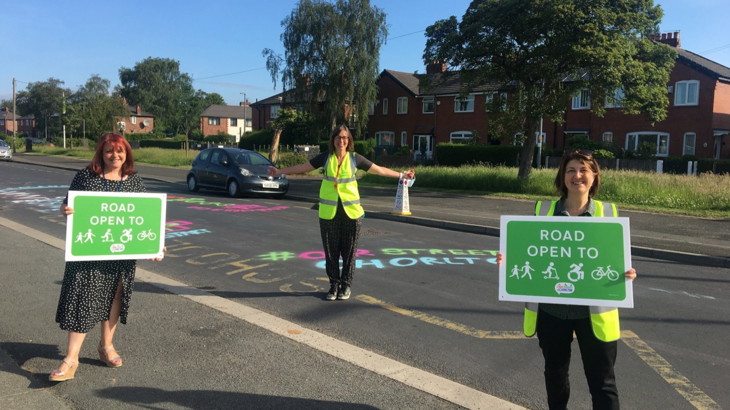 three people standing out in the school street with road open to pedestrians/ bikes/ scooters/wheels etc signs