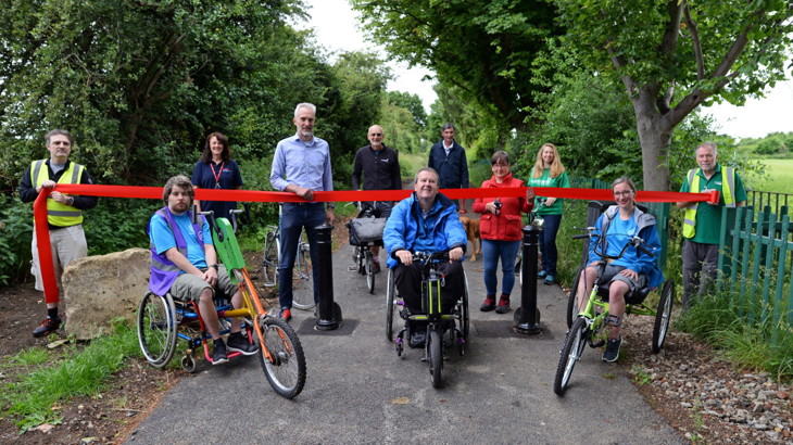 people next to the red ribbon as its being cut along the route