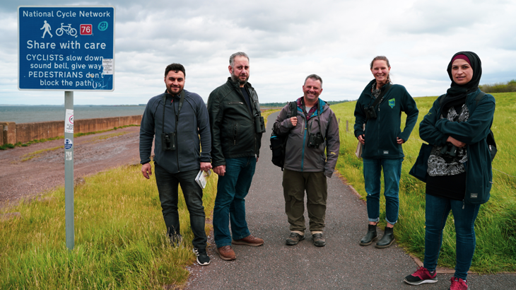 A group of birdwatchers gather by a sign on the National Cycle Network route 76