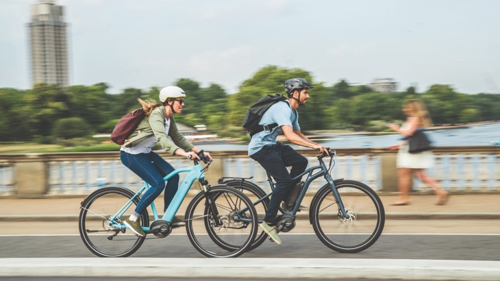 Two people crossing a bridge on e-bikes