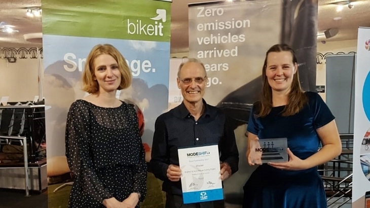 two females and one male stand with best partnership award trophy and certificate at Modeshift National Sustainable Travel awards