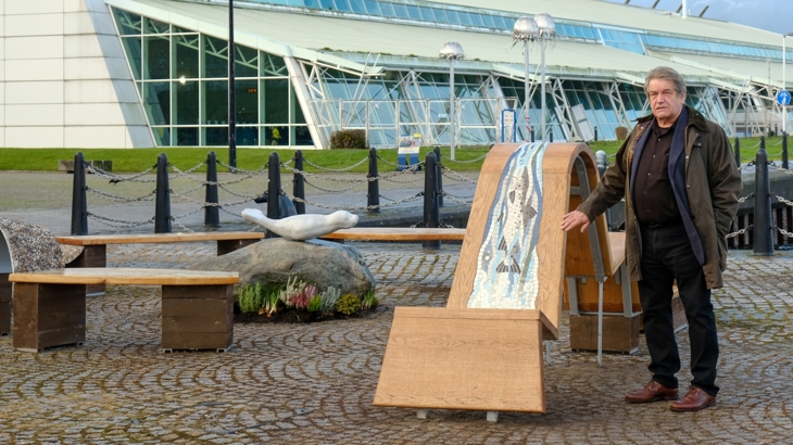 Artist Allan Potter beside his artwork Ebb and Flow, a seating installation featuring mosaics of riverlife with a seal sculpture in the middle.