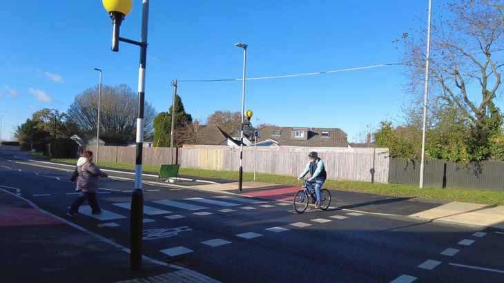 Walking and cycling crossing on road route in use. One person cycling across, while another person walks. 
