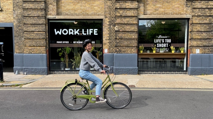 Ying cycles past an urban office space in a quiet street, whilst learning to ride a bike.