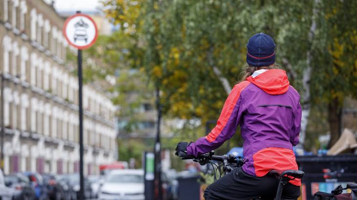A person on a bike wearing a winter coat and hat is standing in a low traffic neighbourhood in London.