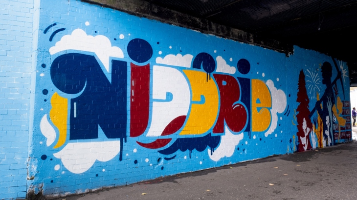 Mural on National Cycle Network Route 1 in Edinburgh. Text reads 'Niddrie' with natural imagery surrounding it, as well as nods to the areas history of mining and brickworks. 