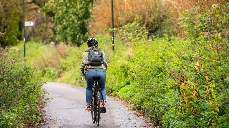 A person on their bike cycling away from the camera down a traffic-free cycle path surrounded by greenery