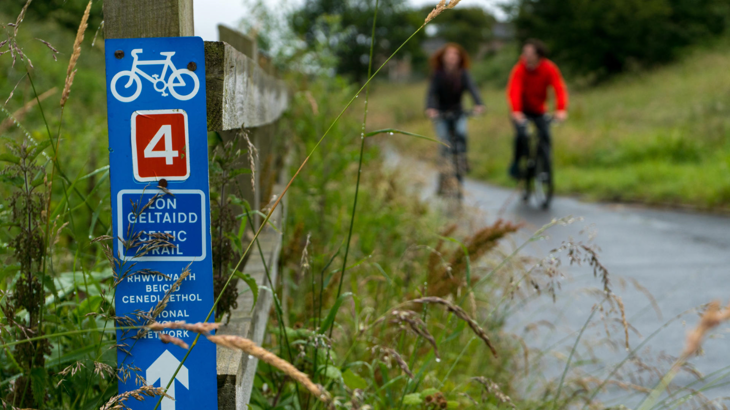A National Cycle Network Route 4 sign in the foreground with two cyclists in the background. 