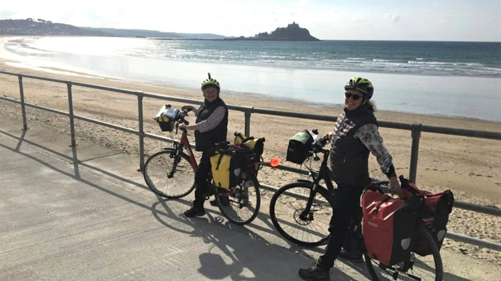 Two women stood with their bicycles and paniers on the sea front on a sunny day in England