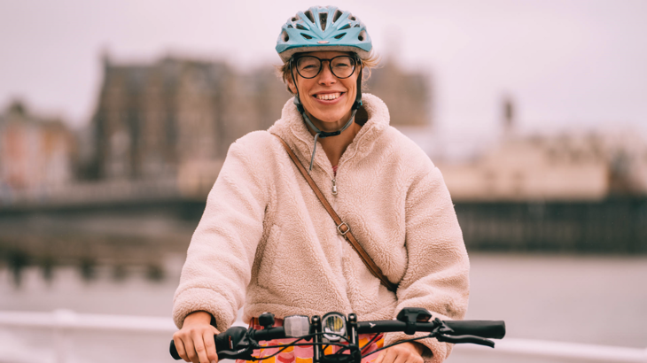 A woman on a bike smiling at the camera. She is stationary on Aberystwyth Promenade.