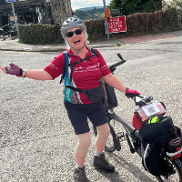 A woman stood with her cycle with a helmet and gloves on on a bright day in the UK 