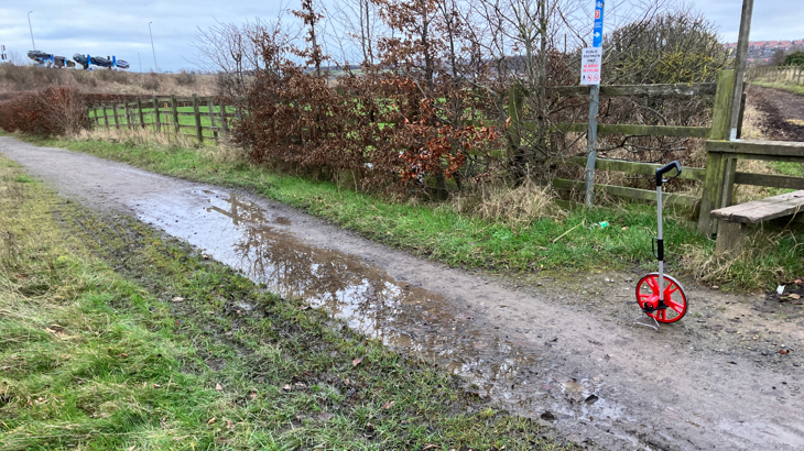 A traffic free National Cycle Network route on a cloudy day with a puddle in the middle of the path 