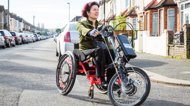 A woman rides a handcycle on a street outside a row of houses