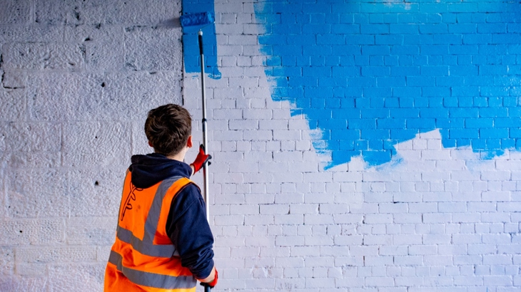 Young artist at work on the new mural in the Niddrie-Bingham tunnel. Photo shows wall being painted blue.
