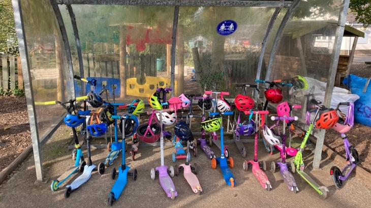 Lots of scooters stored in a shelter in the grounds of a primary school.