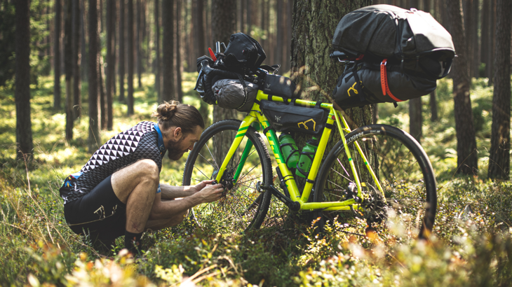 A man fixing his bike in the woods. 